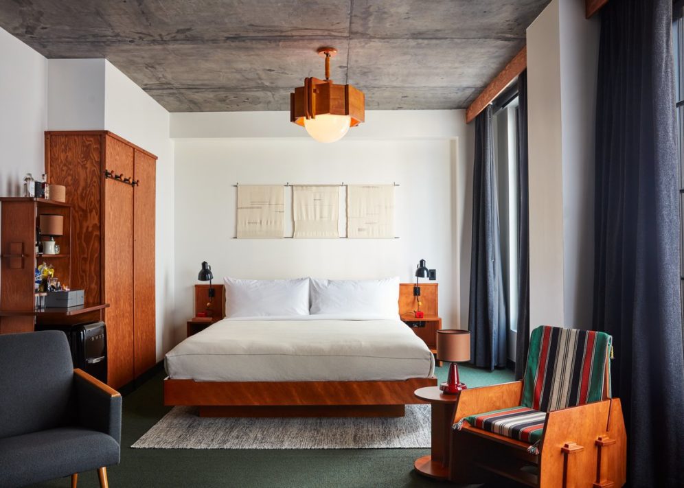 A bed tucked into a corner with bed lamps on each side and a standing closet for hanging clothes