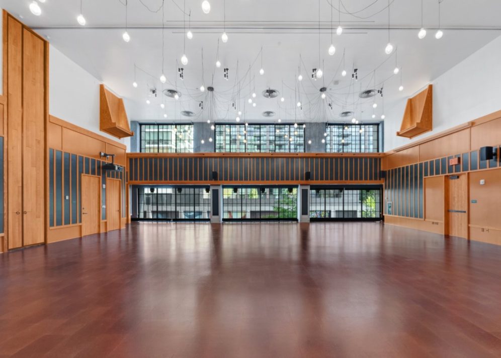 A spacious venue with suspended lights and dark wooden floors overlooks a city street