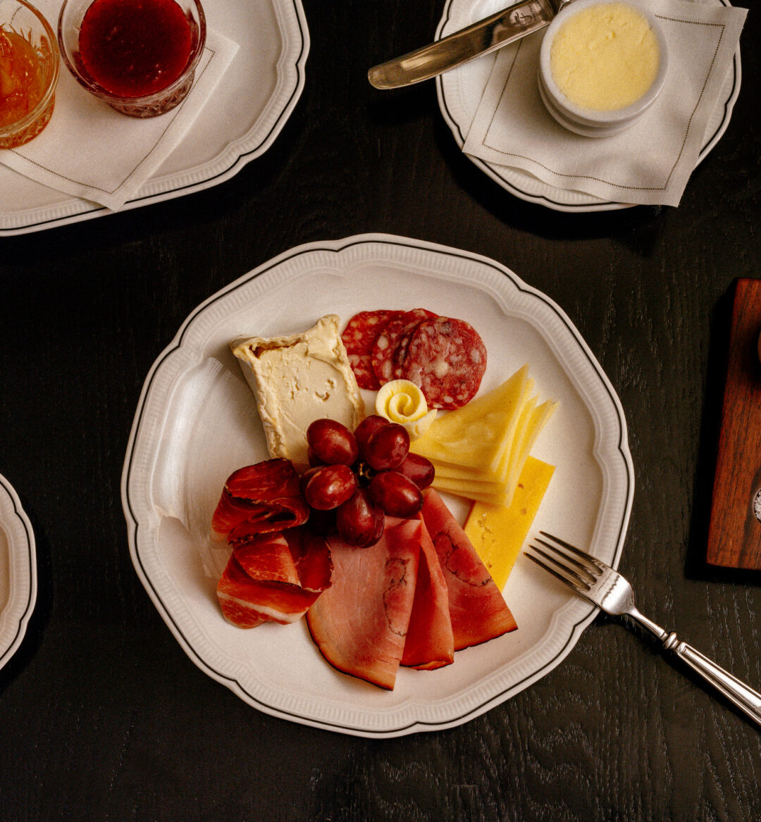 Breakfast served on dining plate with selection of cheeses, croissants and juices.