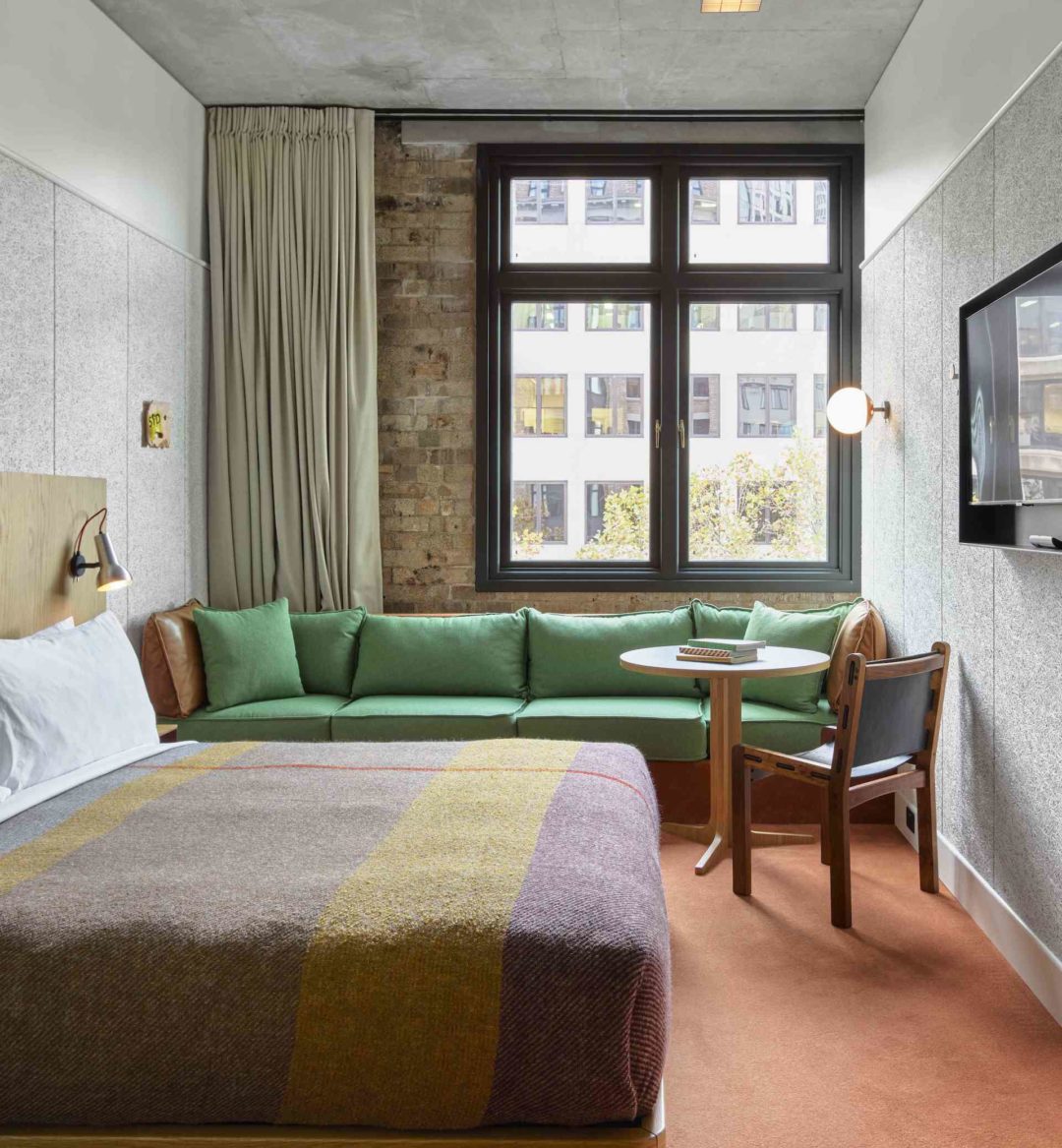 A long, green sofa sits against an exposed brick wall. A table and chair is next to the sofa, providing ample seating space