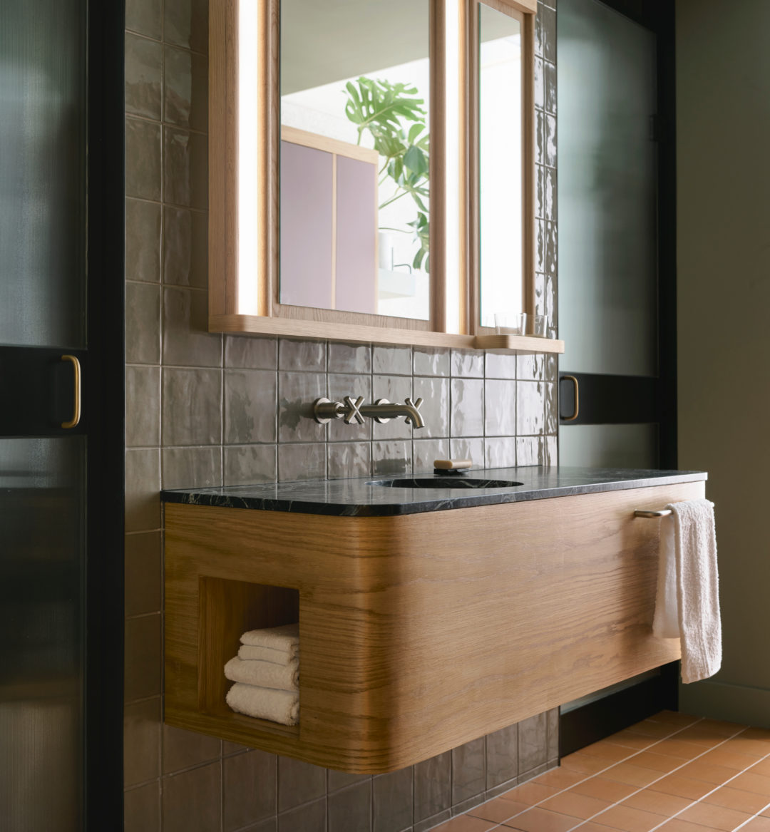 A sleek tiled wall supports to knobs that provide water to a black granite sink