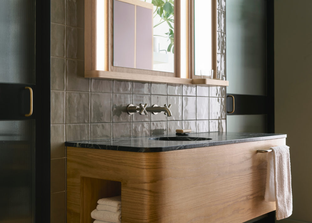 A sleek tiled wall supports to knobs that provide water to a black granite sink