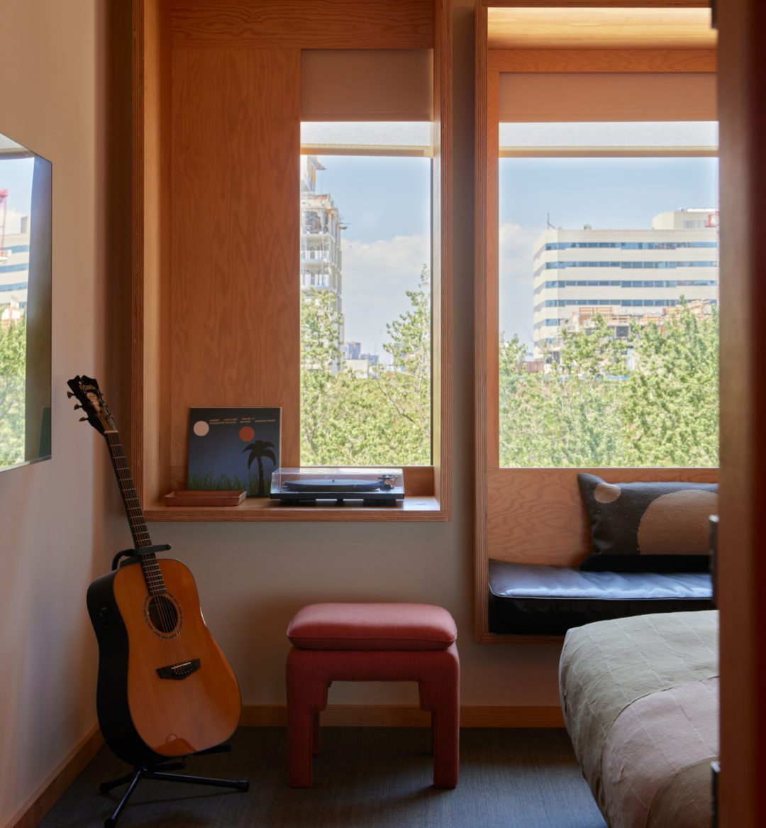A record player and records sit against a window; a red footstool sits on the floor
